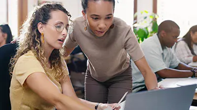 Two women working together on a computer while in an office 